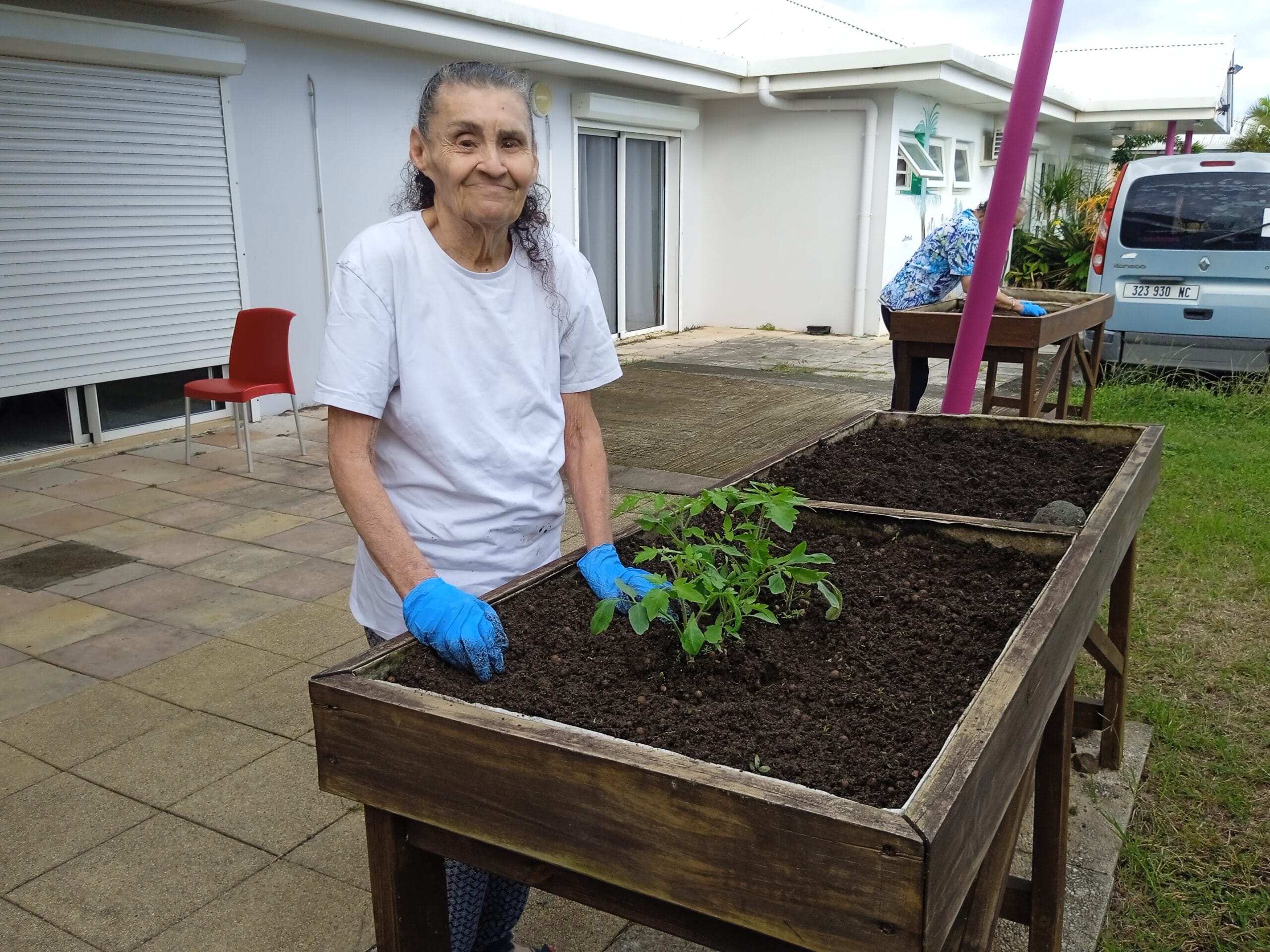 Une résidente de la Résidence La Cordyline participant à une activité de jardinage dans un espace extérieur convivial.